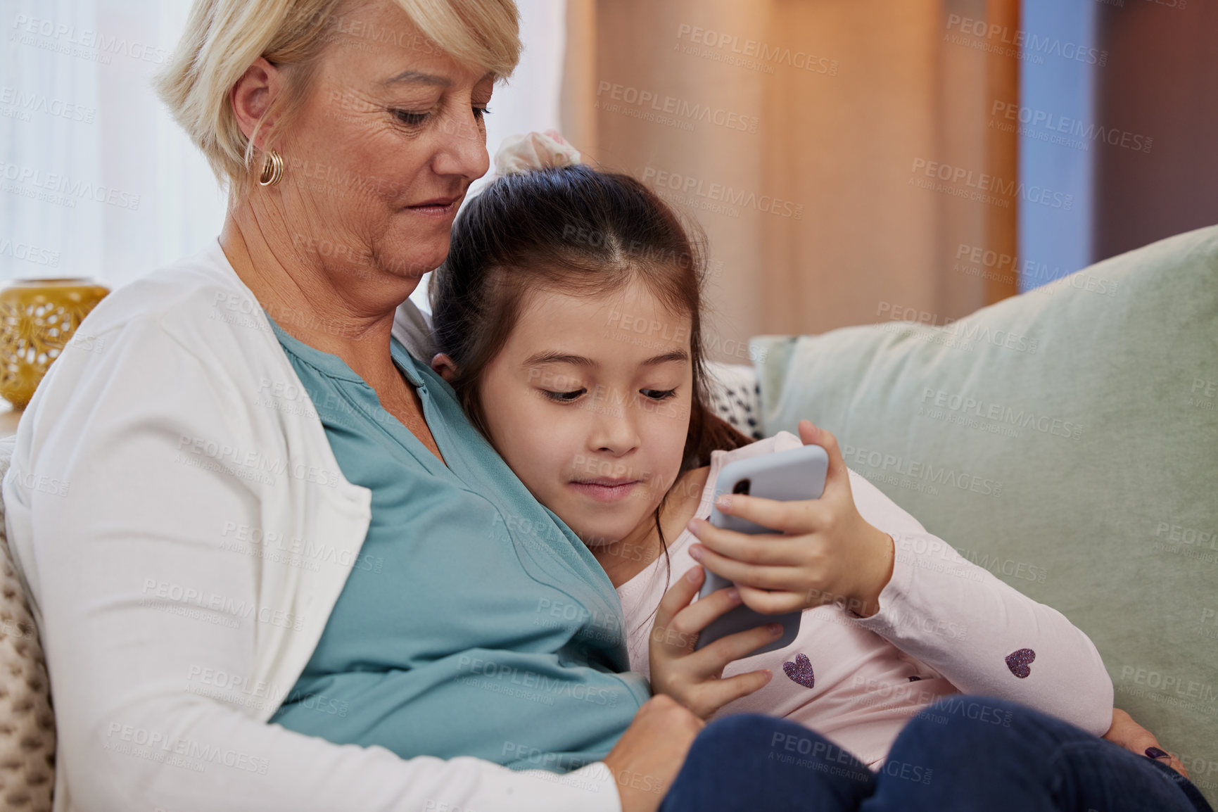 Buy stock photo Family, grandmother and girl child with smartphone on sofa for entertainment on internet or social media. Woman, granddaughter and mobile together on couch for online communication and bonding