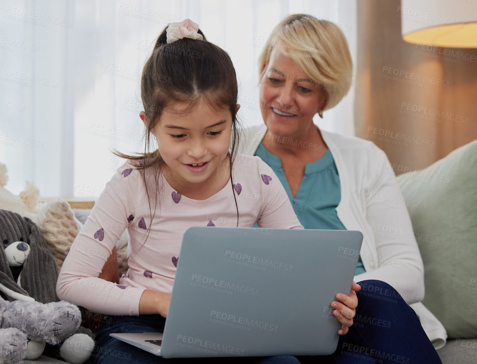 Buy stock photo Shot of an adorable little girl using a laptop while sitting at home with her grandmother