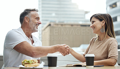 Buy stock photo Shot of two businesspeople shaking hands while having lunch outside an office