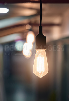 Buy stock photo Shot of a lightbulb hanging from the ceiling in an empty office in the evening