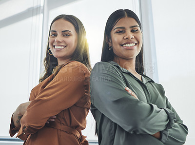 Buy stock photo Cropped portrait of two attractive young businesswomen standing back to back with their arms folded in their office
