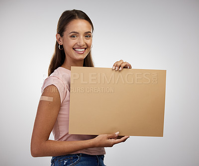 Buy stock photo Shot of a young woman standing alone in the studio and holding a poster after getting vaccinated