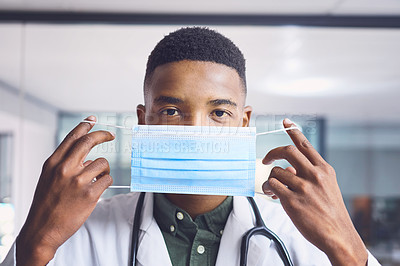 Buy stock photo Cropped portrait of a handsome young male doctor putting on a mask while standing in the hospital