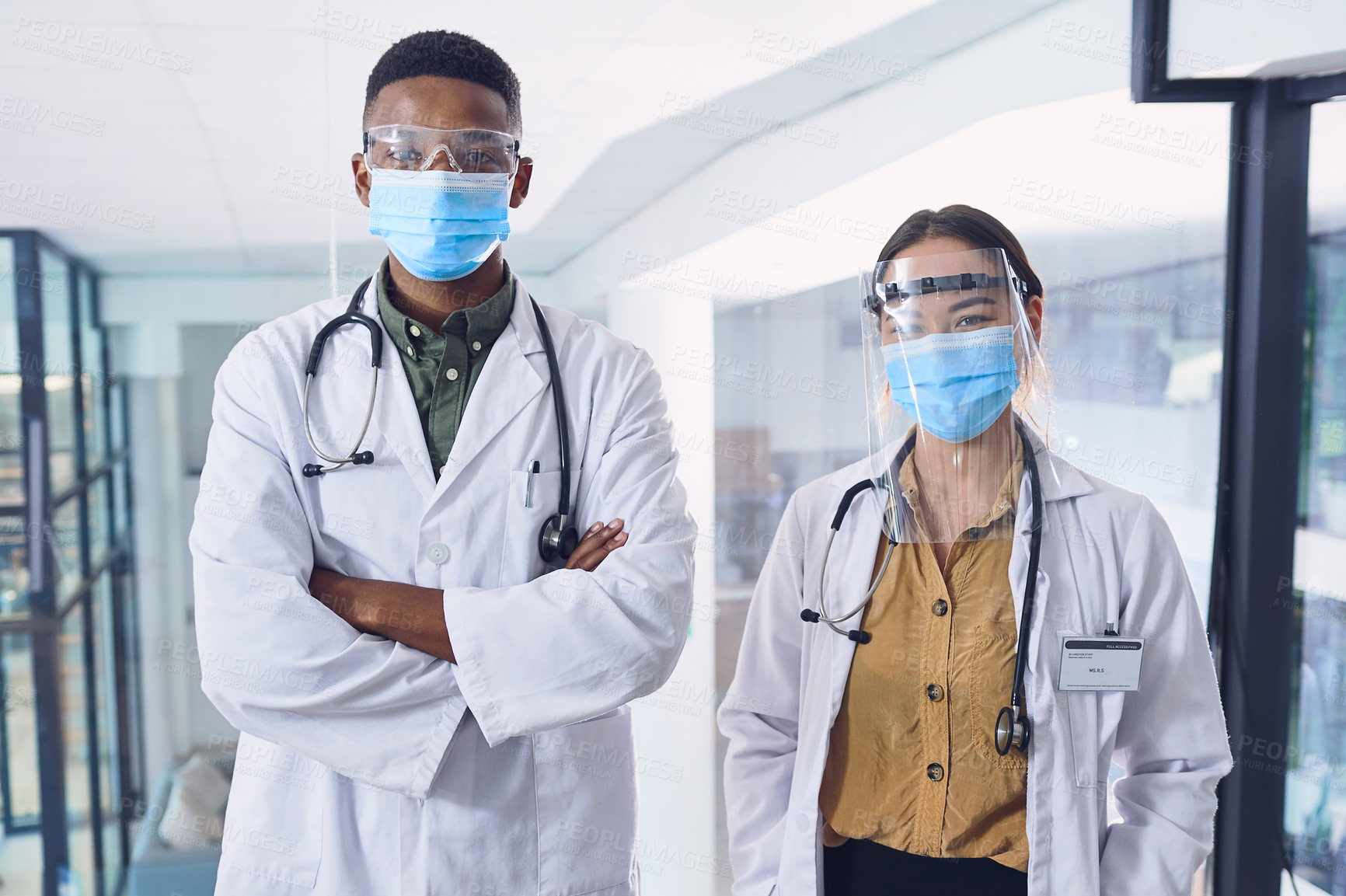 Buy stock photo Cropped portrait of two young doctors wearing masks and other ppe equipment while standing in the hospital