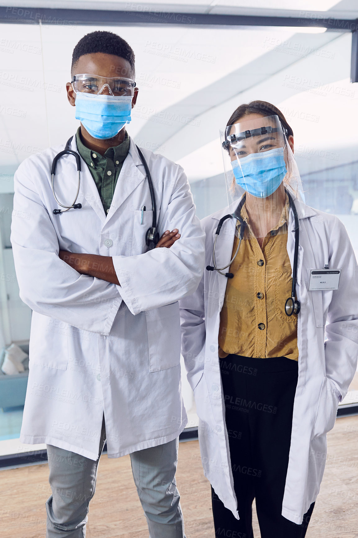 Buy stock photo Cropped portrait of two young doctors wearing masks and other ppe equipment while standing in the hospital