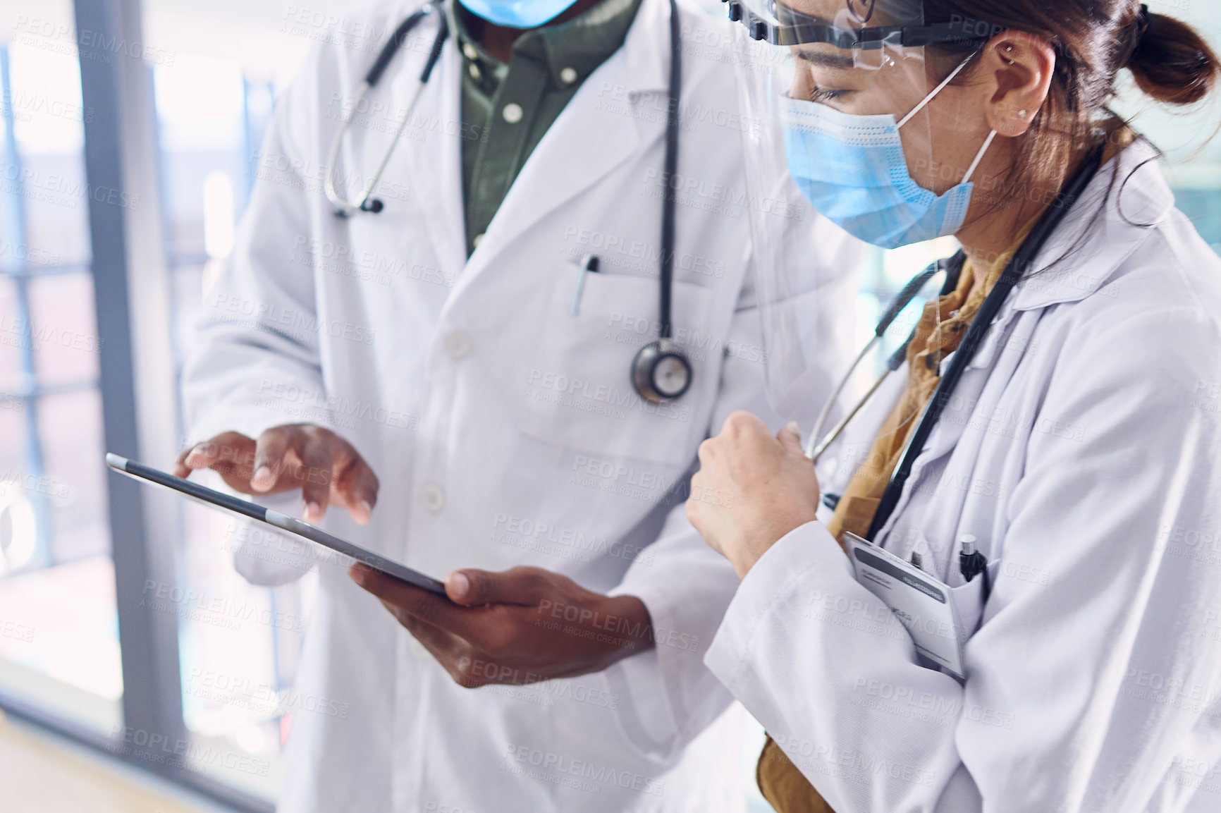 Buy stock photo Cropped shot of two young doctors working on a digital tablet while standing in the hospital