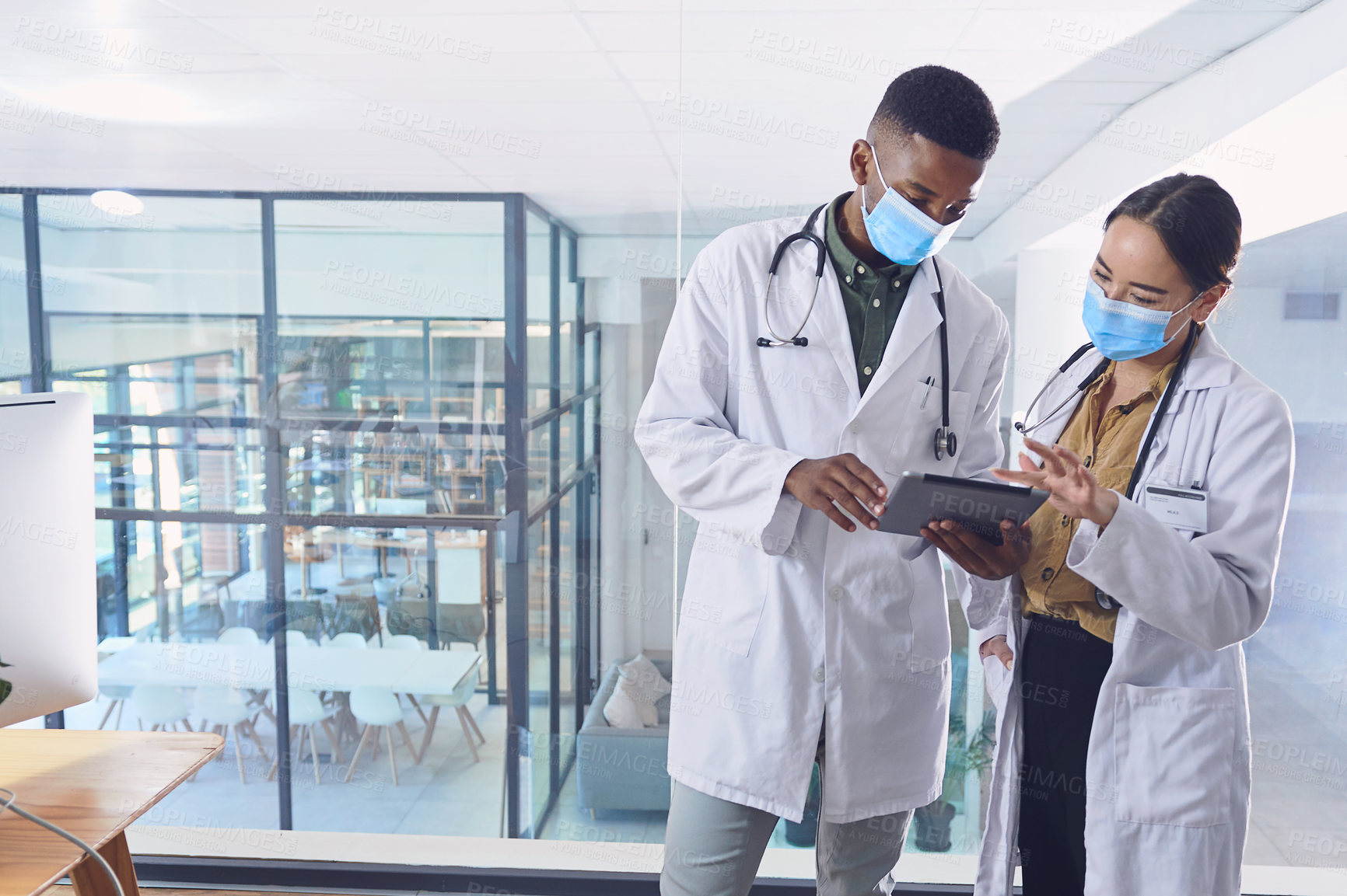 Buy stock photo Cropped shot of two young doctors working on a digital tablet while standing in the hospital