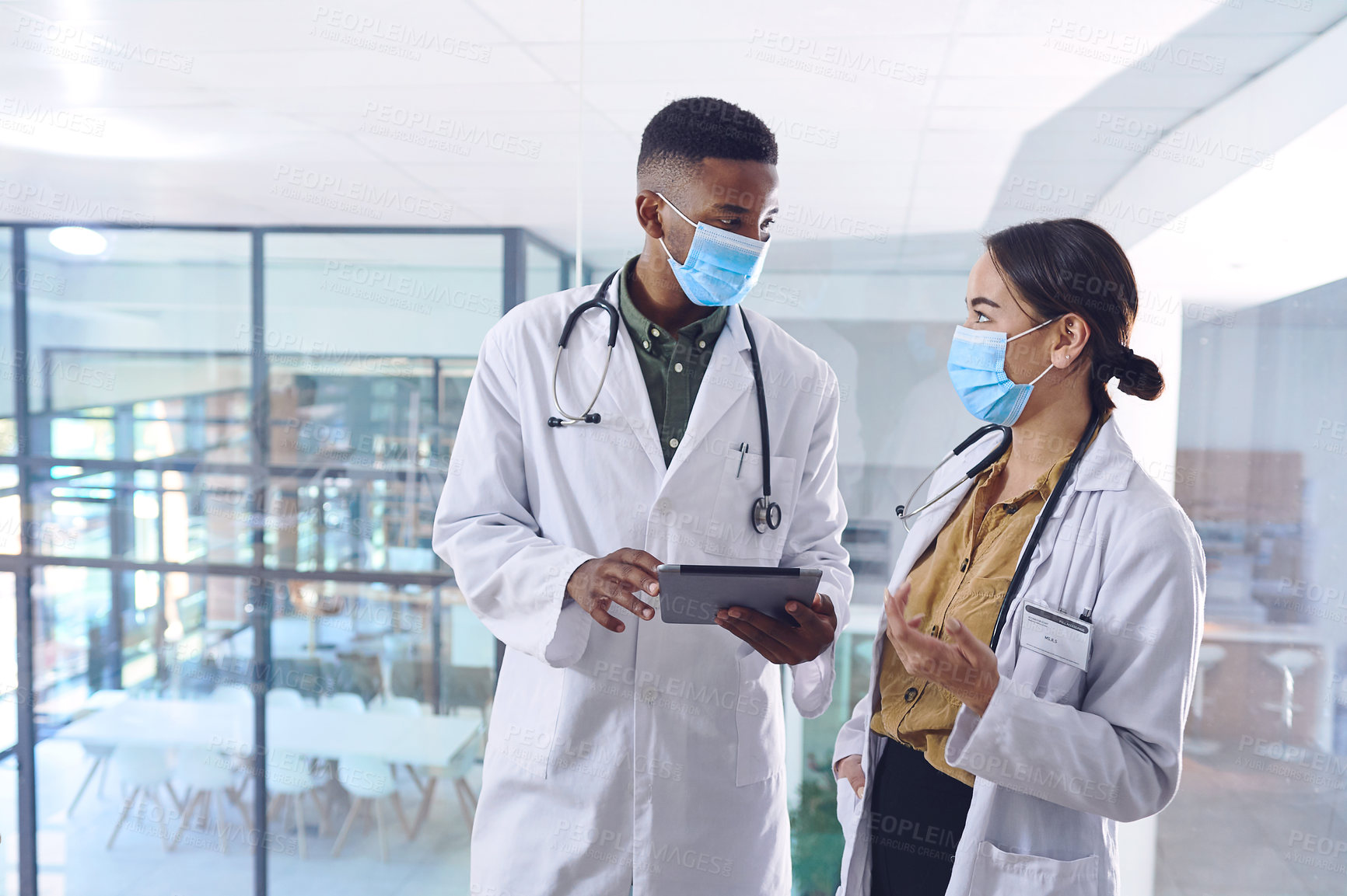 Buy stock photo Cropped shot of two young doctors working on a digital tablet while standing in the hospital