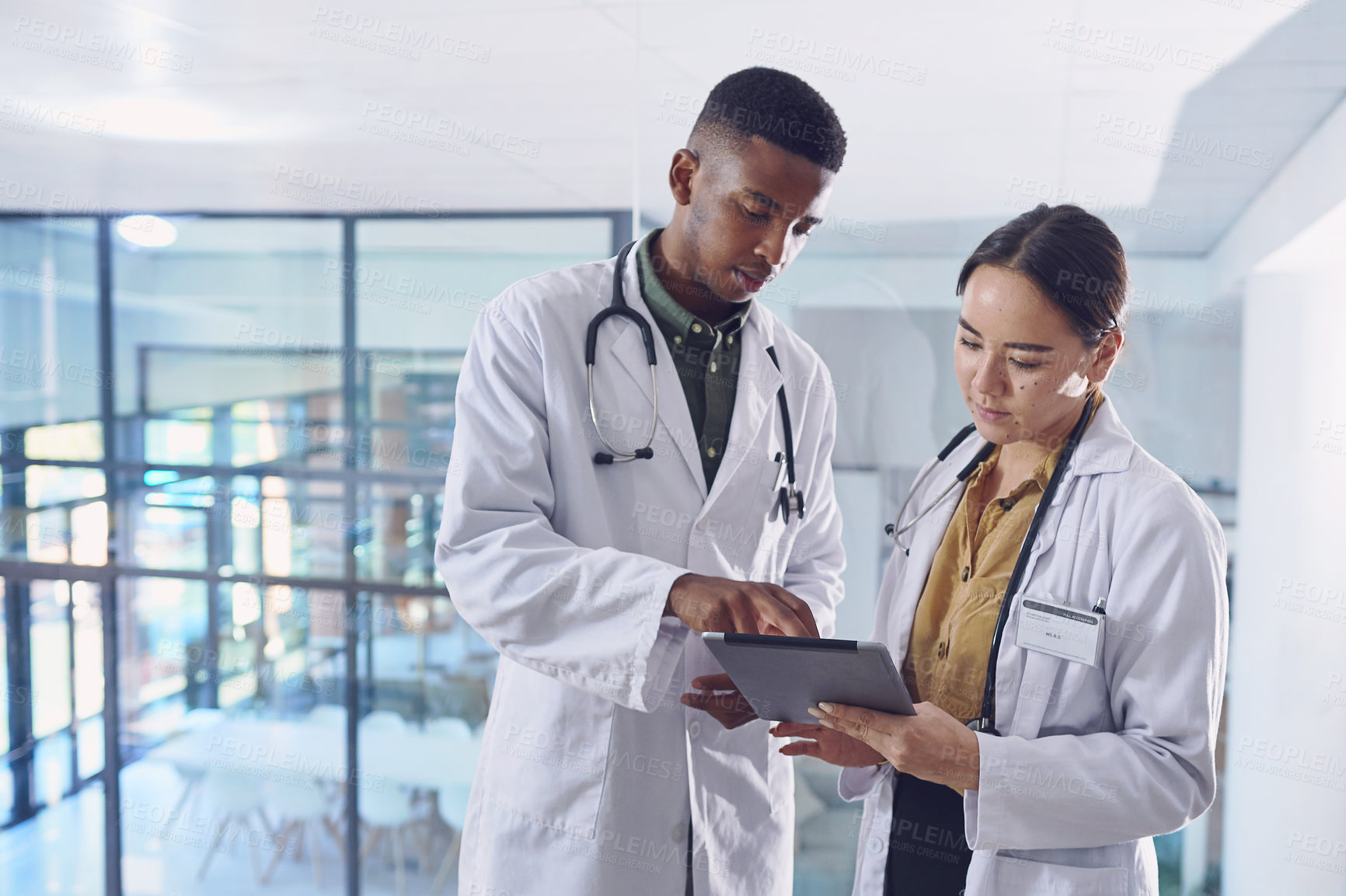 Buy stock photo Cropped shot of two young doctors working on a digital tablet while standing in the hospital