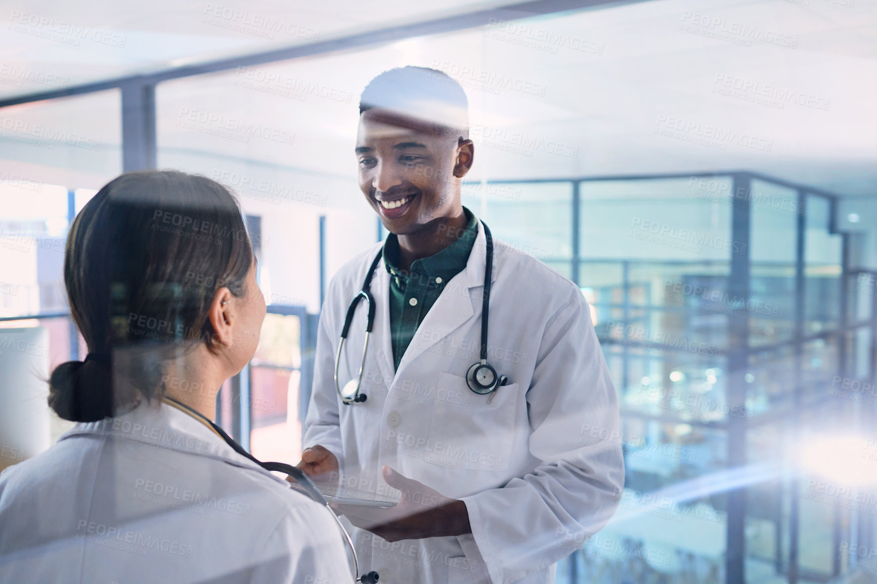 Buy stock photo Cropped shot of two young doctors working on a digital tablet while standing in the hospital