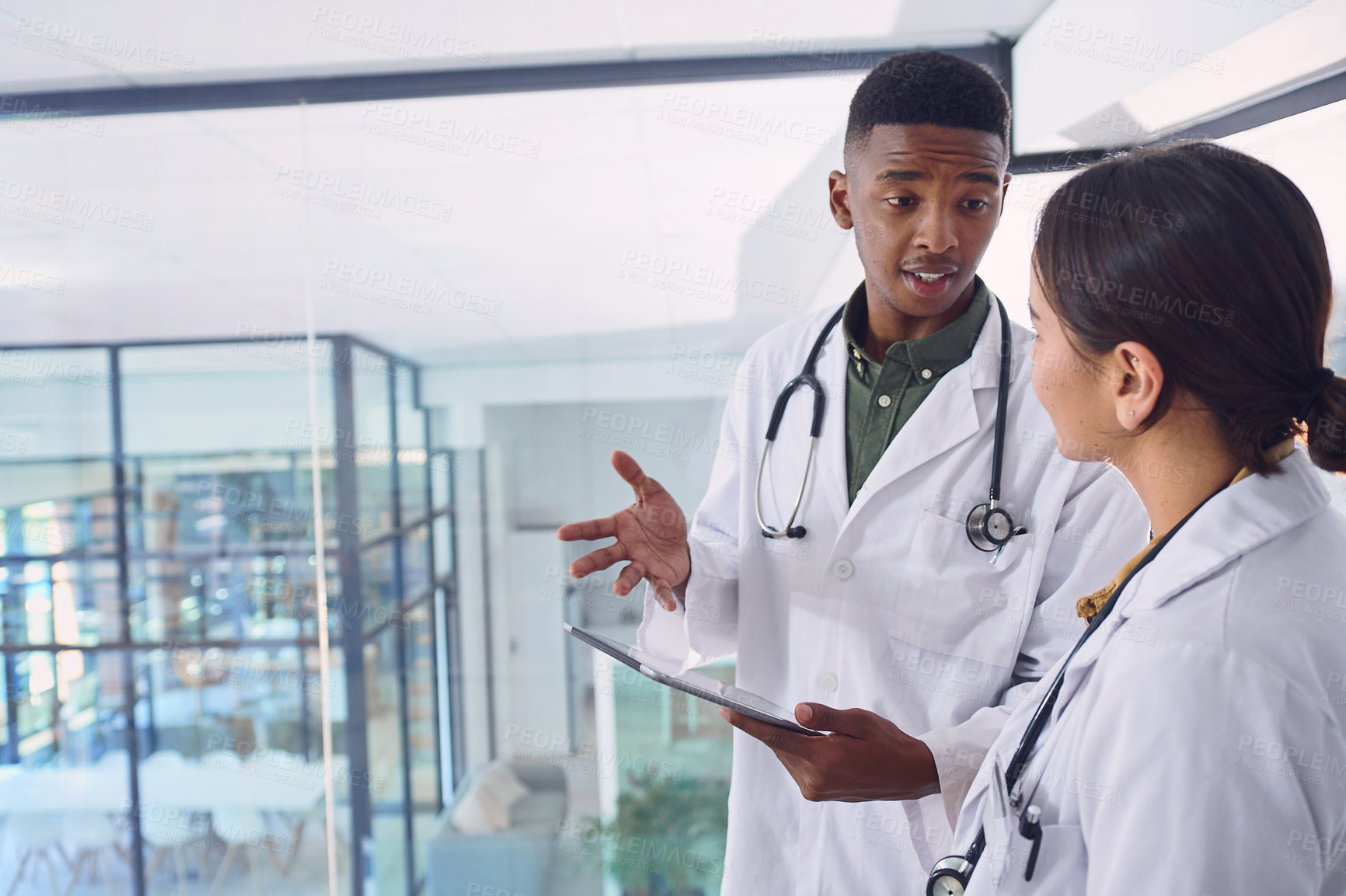 Buy stock photo Cropped shot of two young doctors working on a digital tablet while standing in the hospital