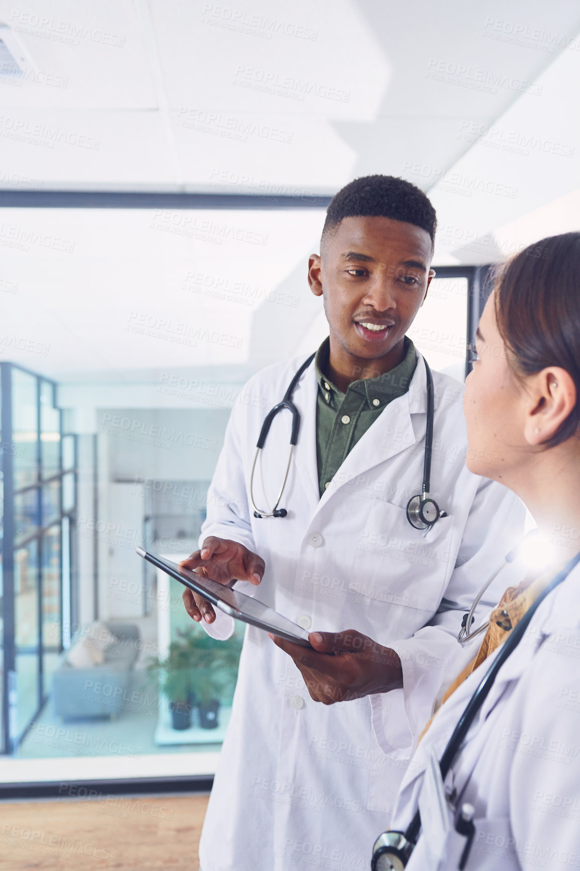 Buy stock photo Cropped shot of two young doctors working on a digital tablet while standing in the hospital