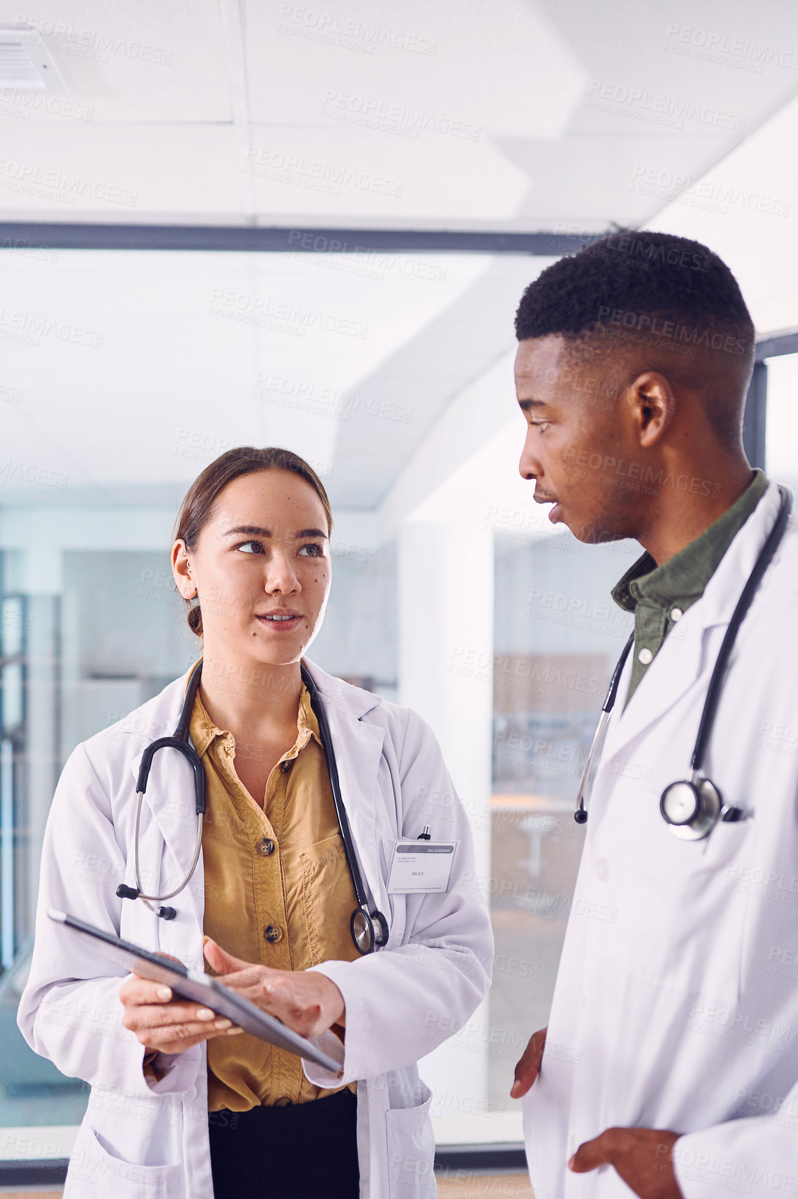 Buy stock photo Cropped shot of two young doctors working on a digital tablet while standing in the hospital