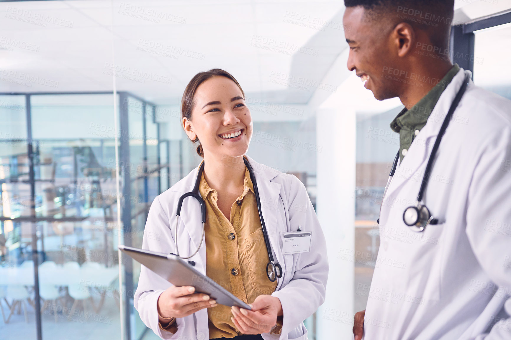 Buy stock photo Cropped shot of two young doctors working on a digital tablet while standing in the hospital