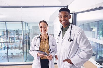 Buy stock photo Cropped portrait of two young doctors working on a digital tablet while standing in the hospital