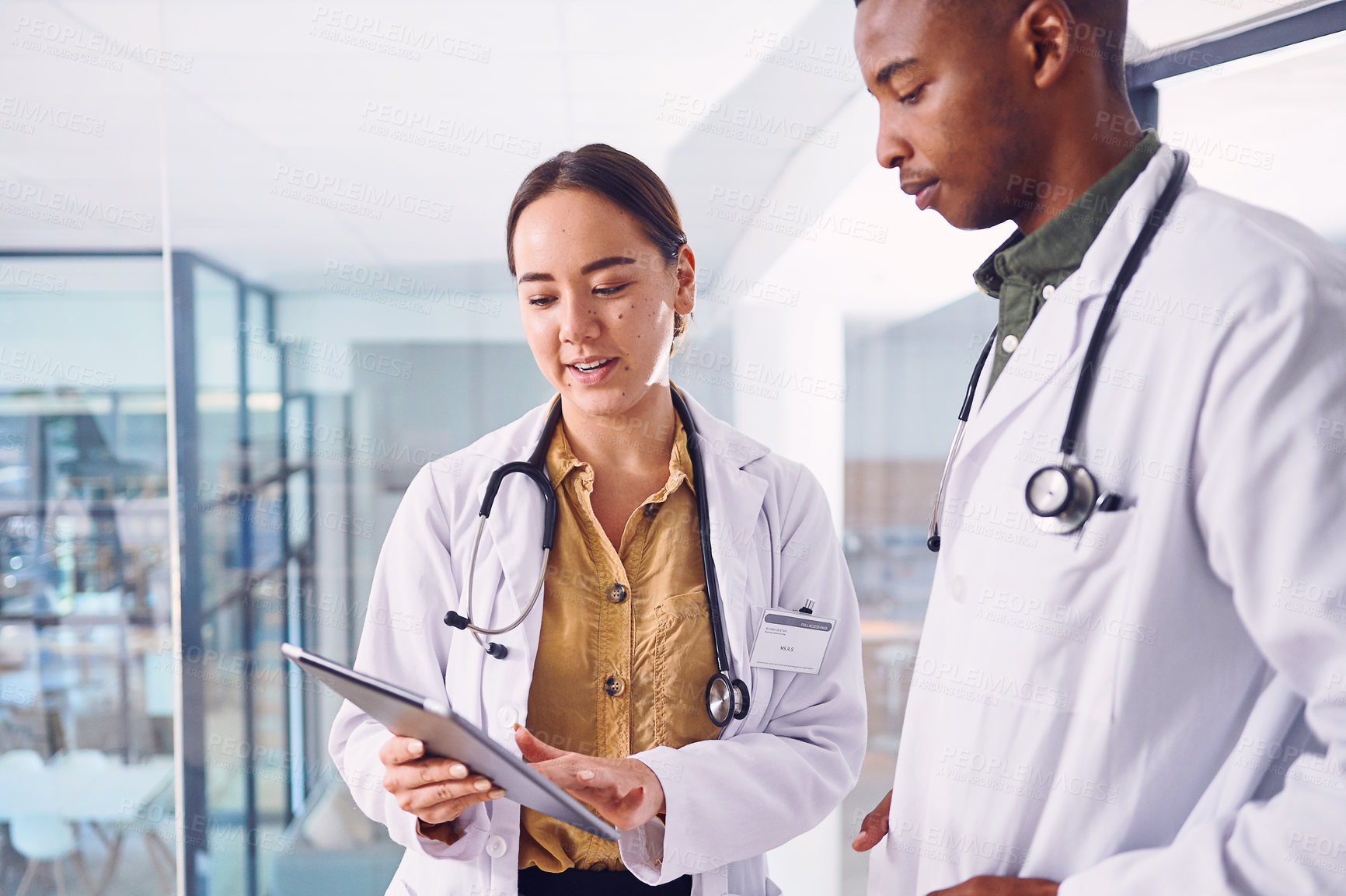 Buy stock photo Cropped shot of two young doctors working on a digital tablet while standing in the hospital