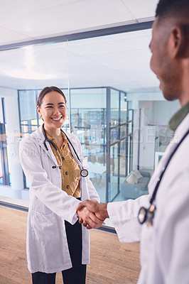 Buy stock photo Cropped shot of two young doctors shaking hands while standing in the hospital