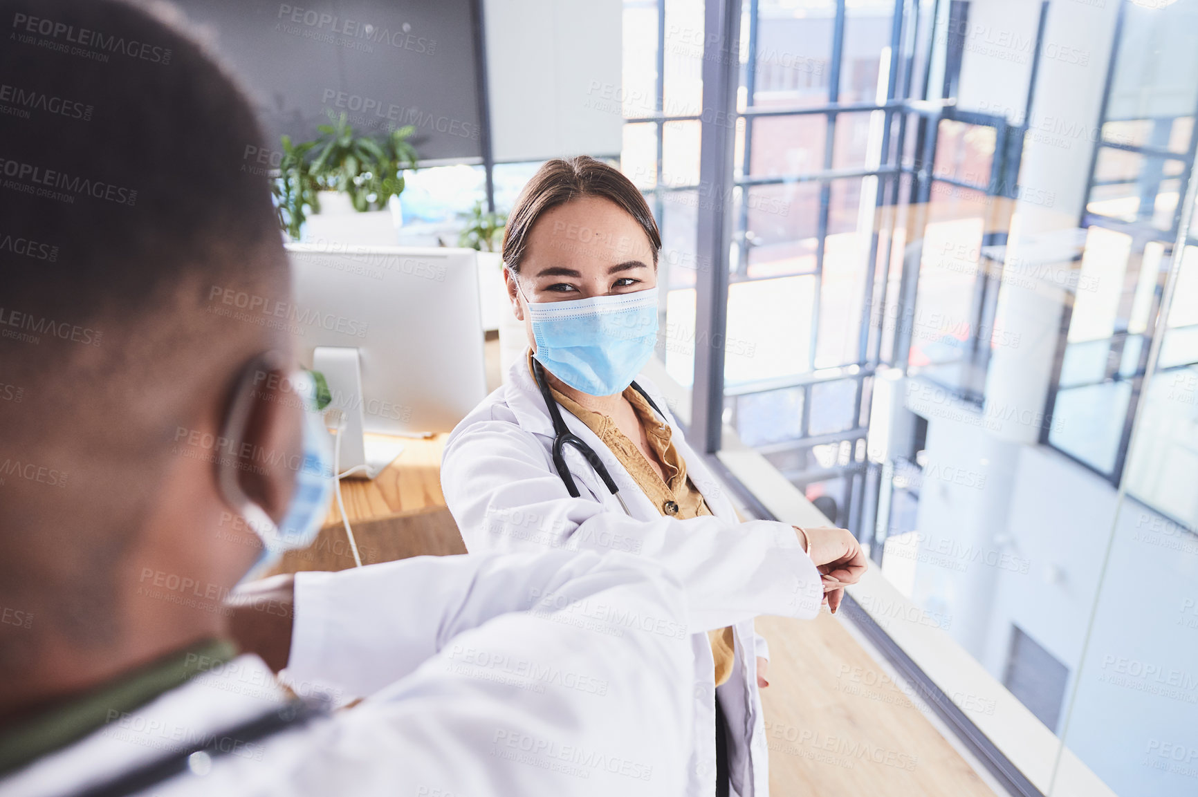 Buy stock photo Cropped shot of two unrecognizable doctors wearing masks and elbow bumping while standing in the hospital