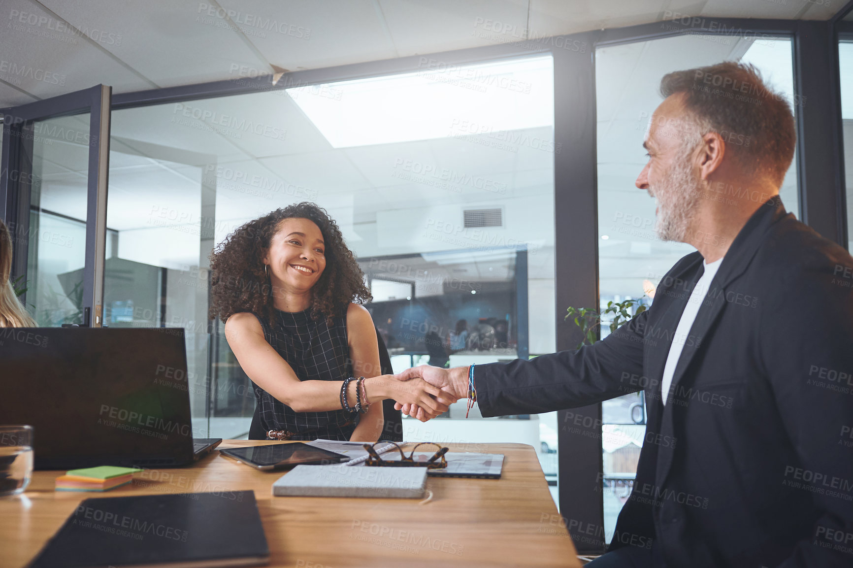 Buy stock photo Shot of two businesspeople sitting together and shaking hands during a meeting in the office