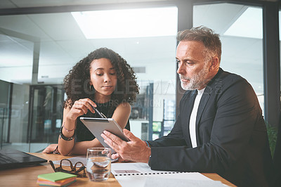 Buy stock photo Shot of two businesspeople sitting together in the office and having a discussion while using a digital tablet