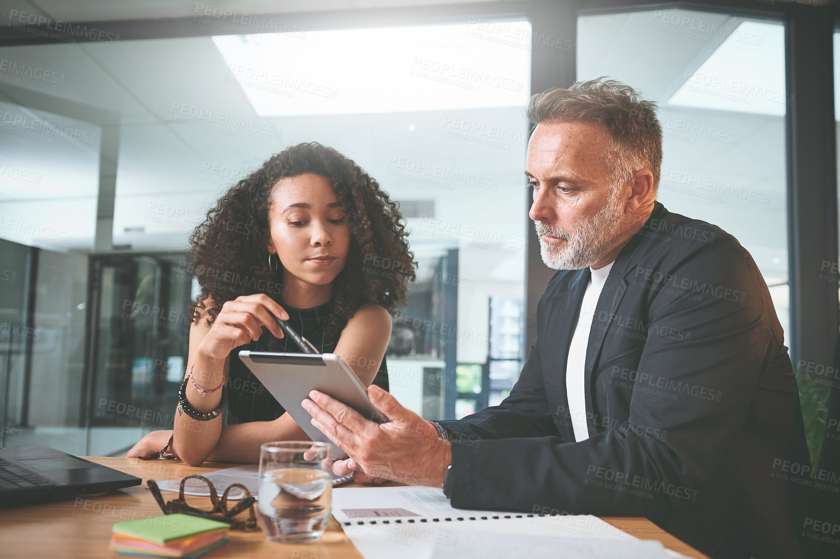 Buy stock photo Shot of two businesspeople sitting together in the office and having a discussion while using a digital tablet