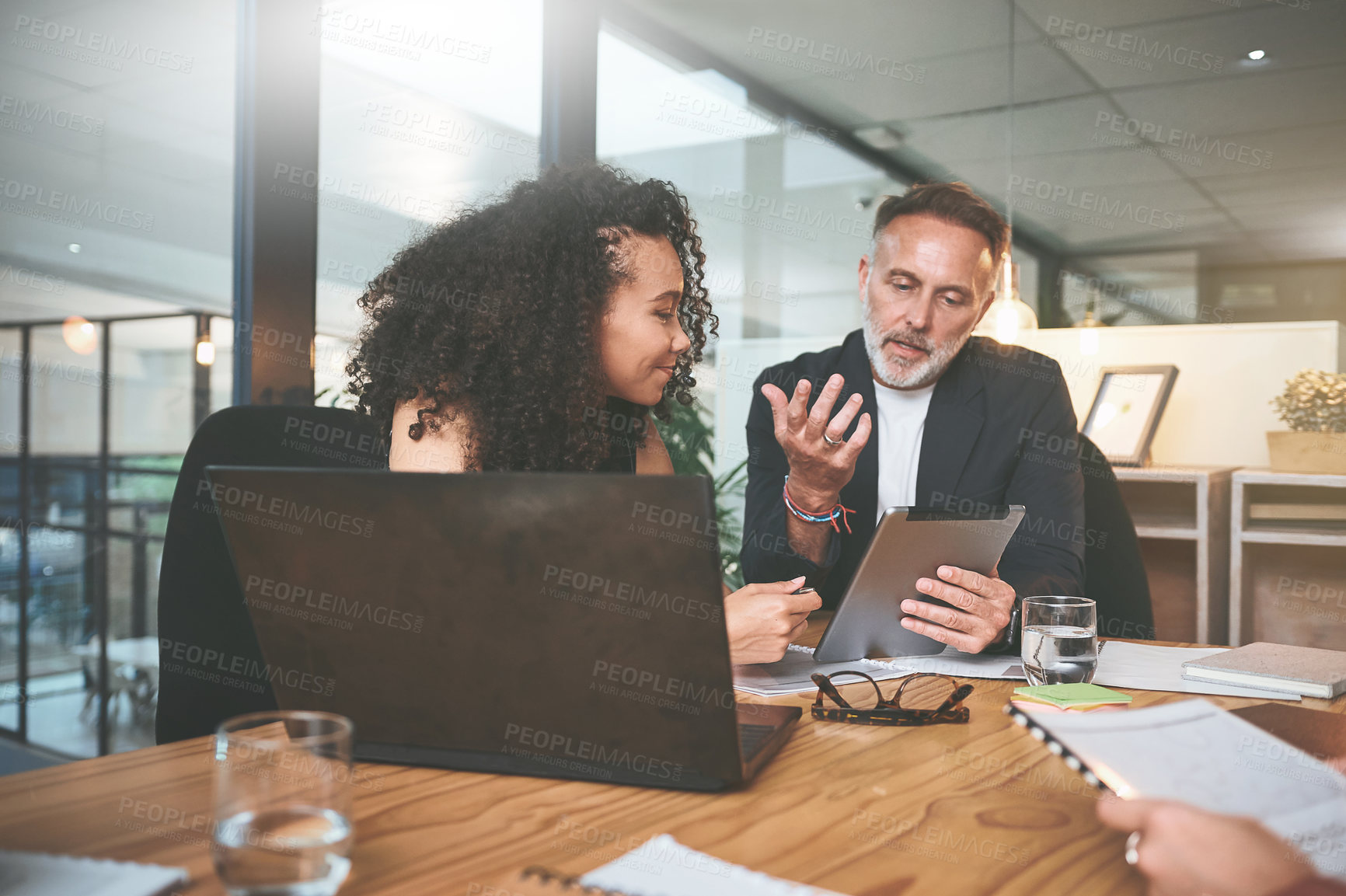 Buy stock photo Shot of two businesspeople sitting together in the office and having a discussion while using a digital tablet