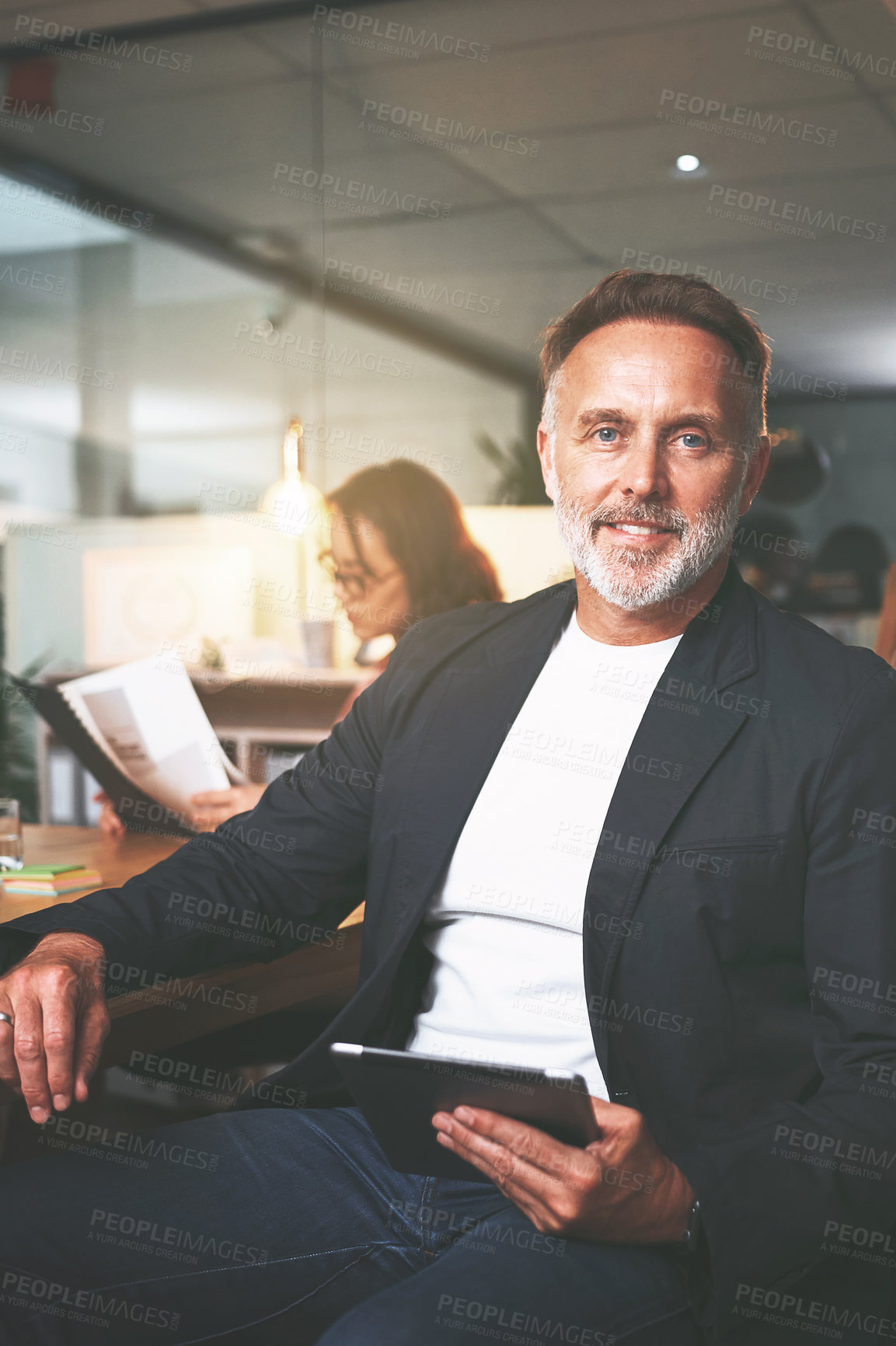 Buy stock photo Shot of a handsome mature businessman sitting and using a digital tablet during a meeting in the office