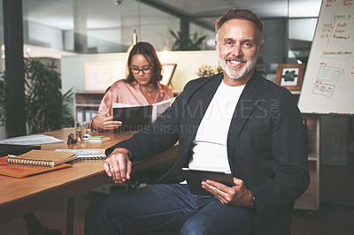 Buy stock photo Shot of a handsome mature businessman sitting and using a digital tablet during a meeting in the office