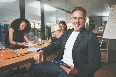 Buy stock photo Shot of a handsome mature businessman sitting and using a digital tablet during a meeting in the office