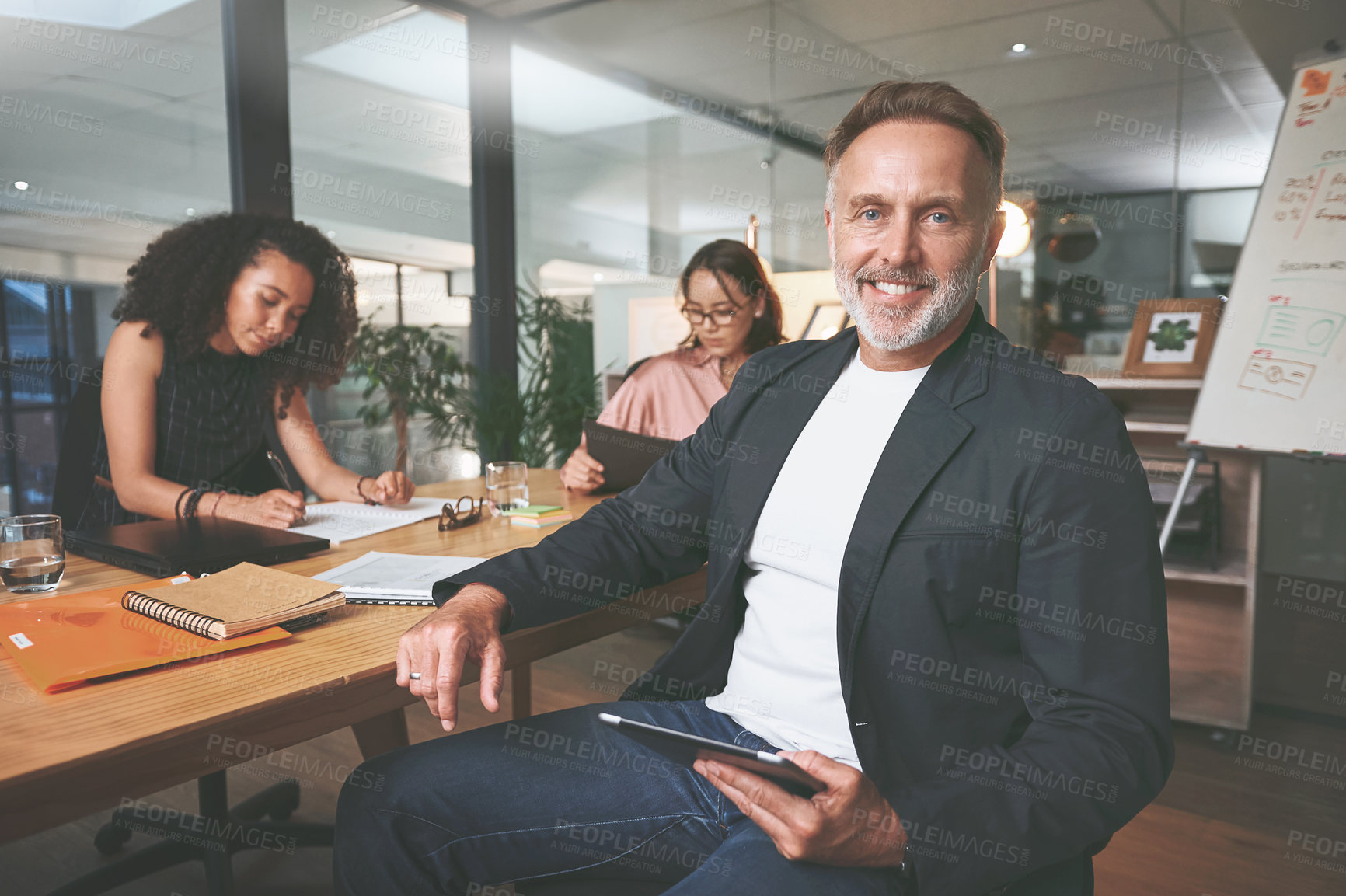 Buy stock photo Shot of a handsome mature businessman sitting and using a digital tablet during a meeting in the office