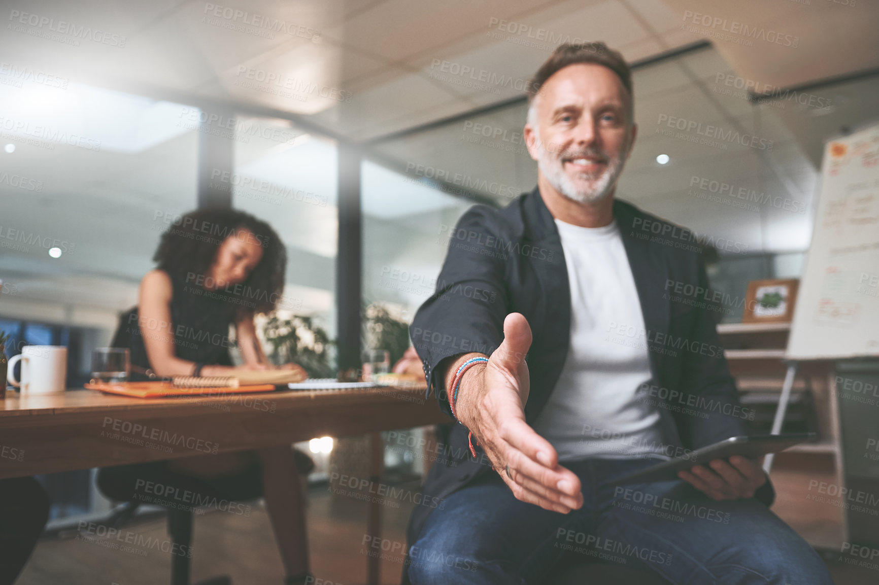 Buy stock photo Shot of a handsome mature businessman sitting in the office and extending his hand out for a handshake