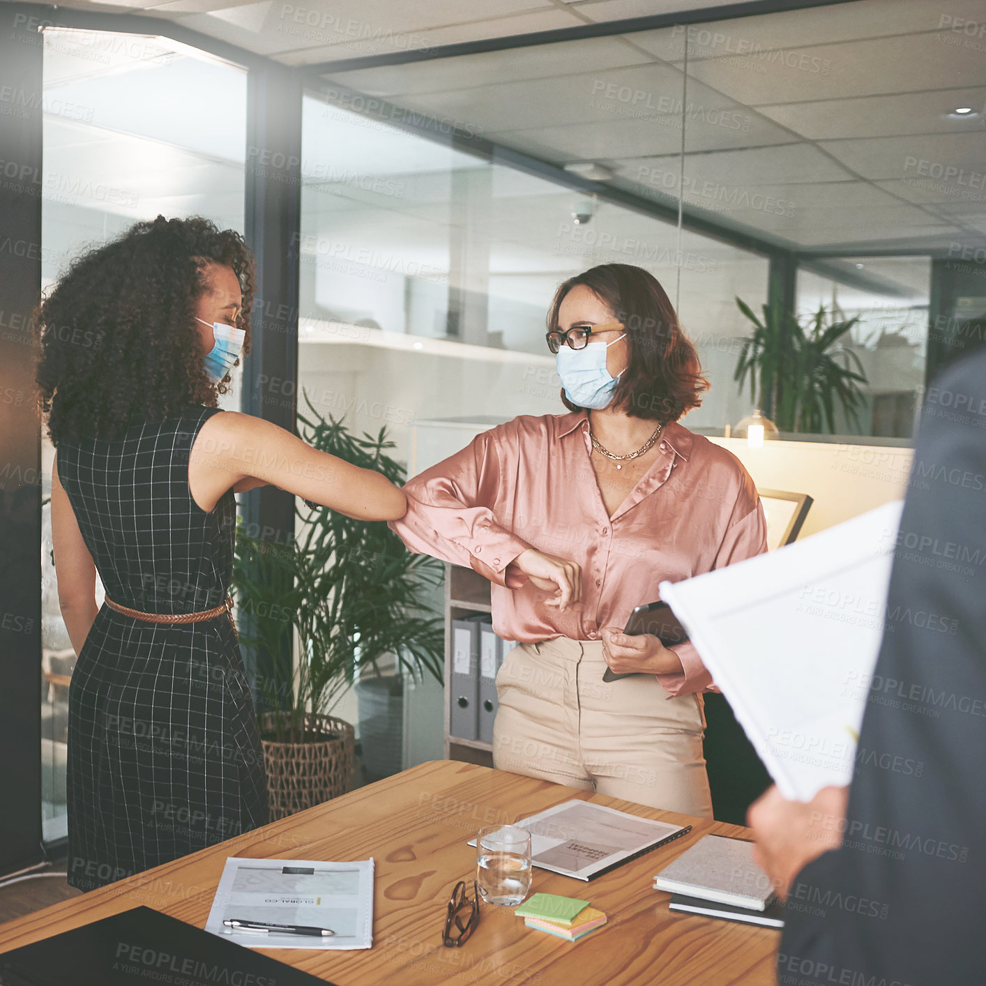 Buy stock photo Shot of two businesswomen standing together and elbowing each other and wearing face masks during a meeting in the office