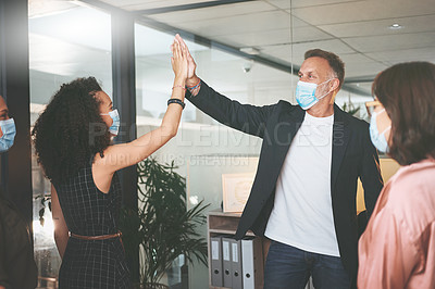 Buy stock photo Shot of two businesspeople standing together and giving each other a high five while wearing masks in the office