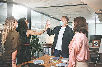 Buy stock photo Shot of businesspeople standing together and giving each other a high five while wearing masks in the office