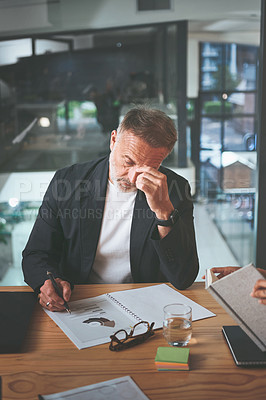 Buy stock photo Shot of a handsome mature businessman sitting alone in the office and feeling stressed while reading paperwork