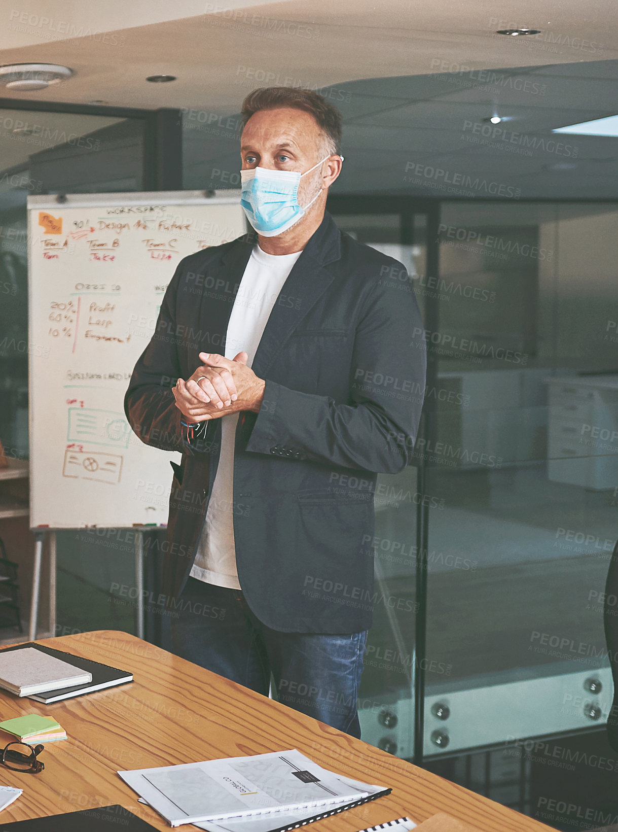 Buy stock photo Shot of a handsome mature businessman standing in the office and giving a presentation while wearing a face mask