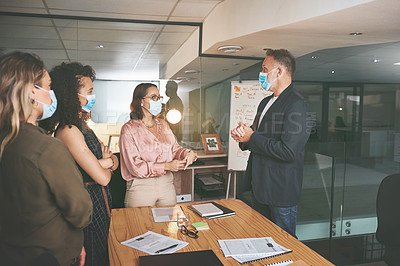 Buy stock photo Shot of a diverse group of businesspeople having a discussion during a meeting in the office while wearing face masks