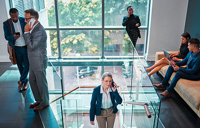 Buy stock photo Shot of a mature businesswoman walking up the stairs while using a phone in a busy office at work