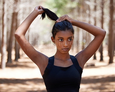 Buy stock photo Shot of an attractive young woman standing alone outside and tying her hair before her workout