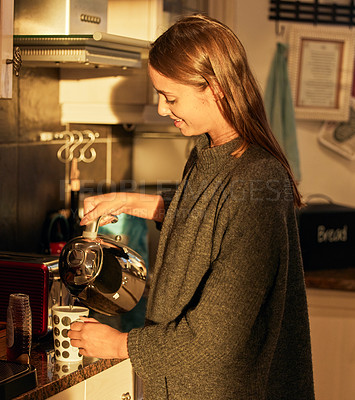 Buy stock photo Shot of a young woman pouring hot water from a kettle into a mug at home