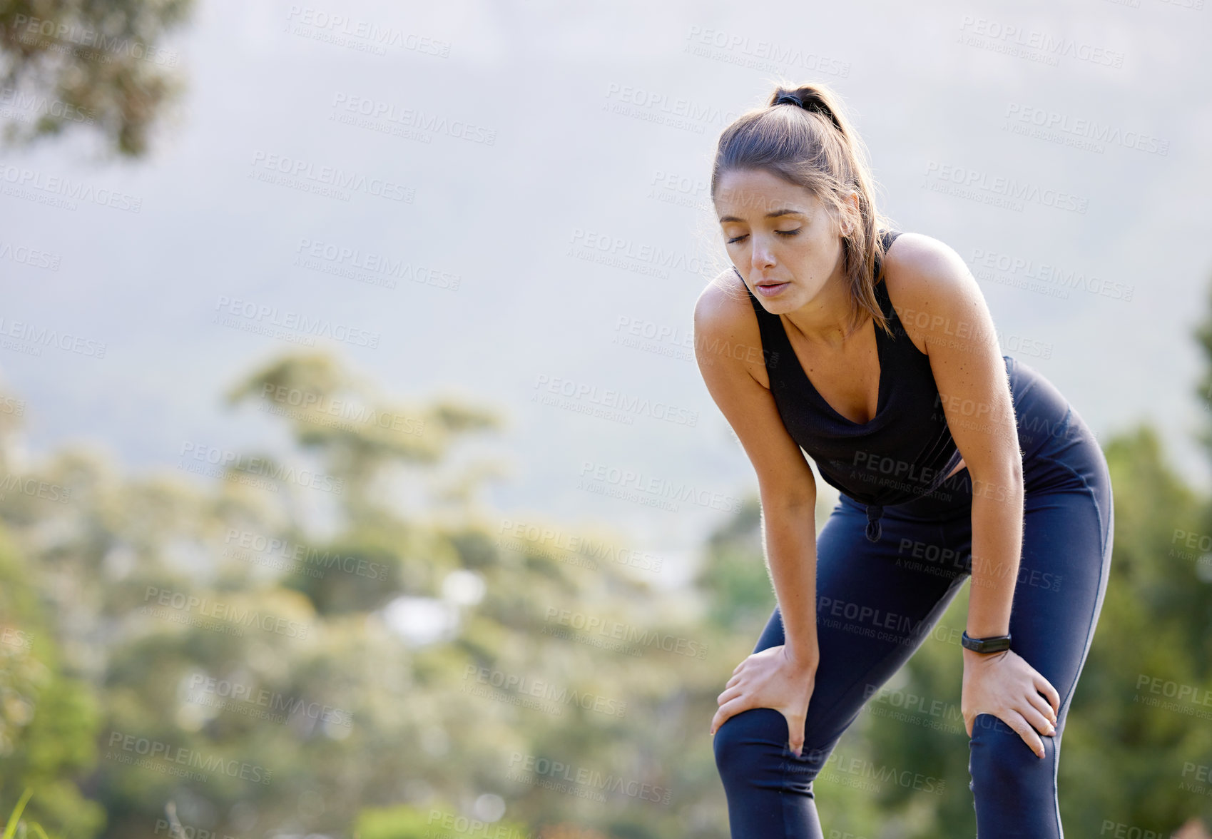 Buy stock photo Shot of a sporty young woman catching her breath while exercising outdoors