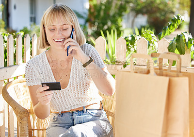 Buy stock photo Shot of a woman holding her credit card and talking on her cellphone while sitting outside with shopping bags