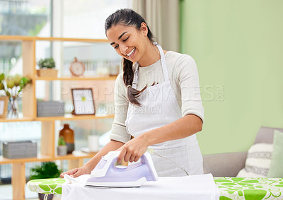Buy stock photo Shot of an attractive young woman standing and ironing clothes at home