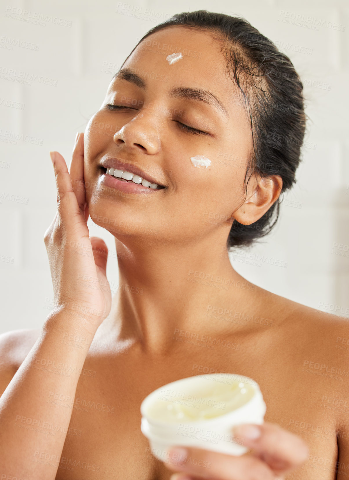 Buy stock photo Shot of young woman using with facial moisturiser at home