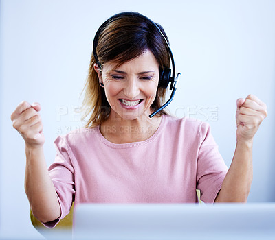 Buy stock photo Shot of a mature call centre agent cheering while working on a laptop in an office