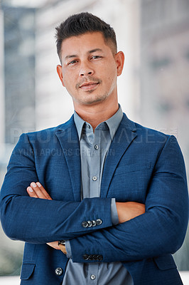 Buy stock photo Shot of a handsome young businessman standing alone in the office with his arms folded