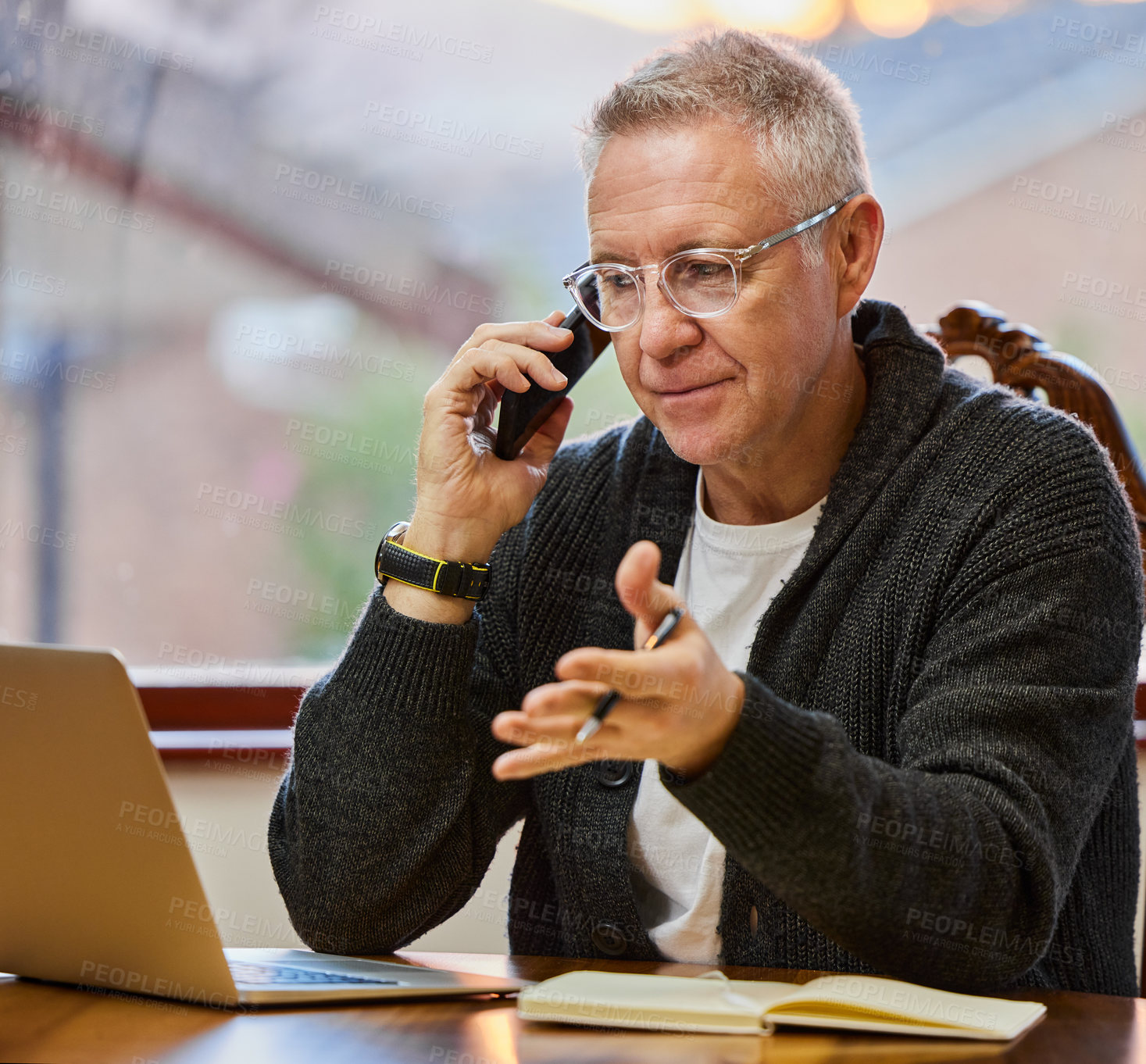 Buy stock photo Cropped shot of a handsome senior man making a phonecall while working on his laptop in the study