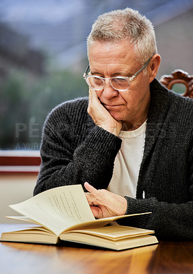 Buy stock photo Reading, glasses and senior man with book by dining room table for knowledge at retirement home. Spectacles, serious and elderly male person enjoying novel, story or literature at modern house.