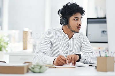 Buy stock photo Shot of a young businessman writing notes while working on a computer in an office