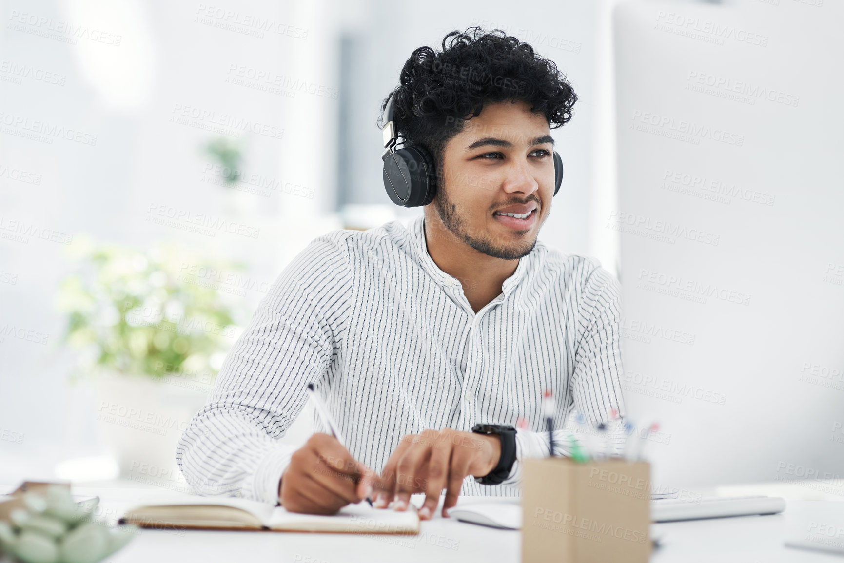 Buy stock photo Shot of a young businessman writing notes while working on a computer in an office